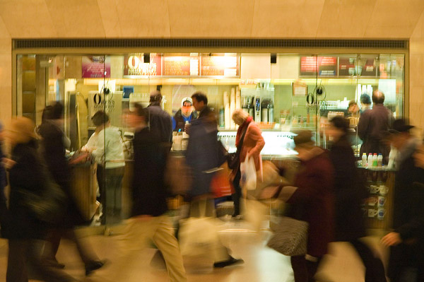 People rushing quickly past a coffee counter.