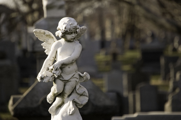 A sculpture of a cherub, bearing flowers, atop a tombstone.