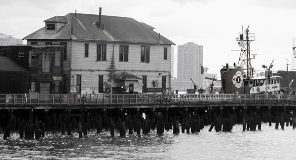 A building and a tug boat on a pier in the Hudson.
