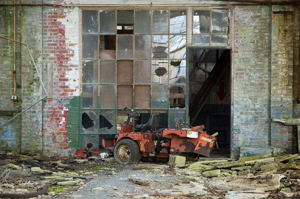 An abandoned red vehicle sits amid broken glass, exposed
brick, and loose cinder blocks.
