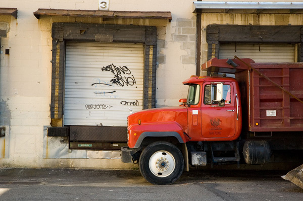 A red truck is parked by a closed loading dock
door.
