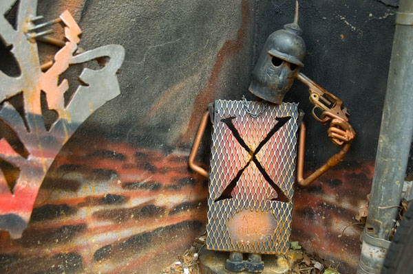 A sculpted metal knight holds a revolver to his head.