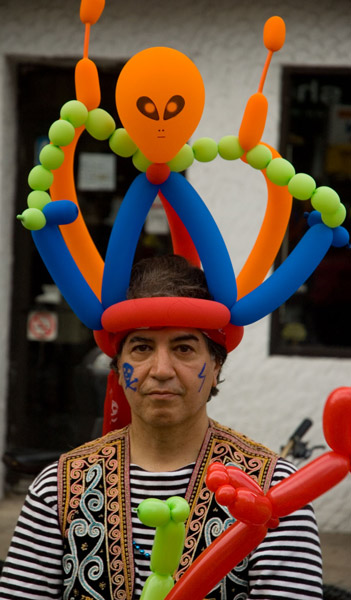 A street performer wears a headdress of colorful balloons.