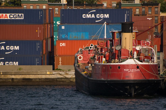 A red tugboat is docked in front of colored shipping
containers.