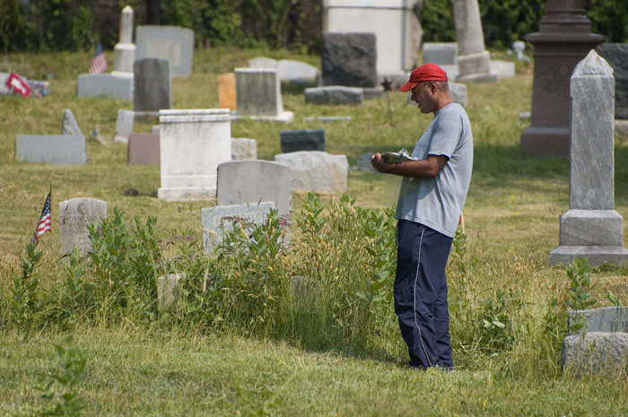 A man with a clipboard lists tombstones and locations.
