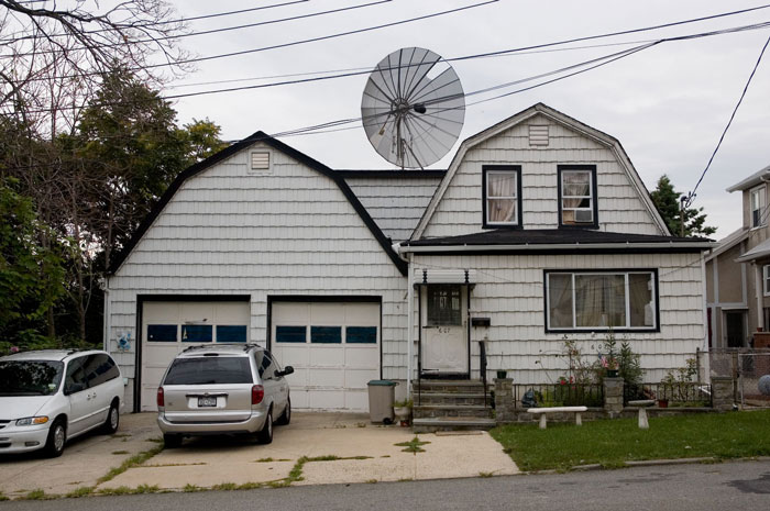 Two cars parked in front of a white, wood frame house.