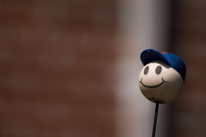 A car antenna is topped with a smiling sphere in a Mets cap.