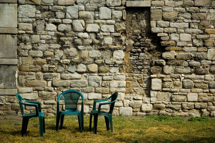 Chairs sit on a grass space in front of a rugged stone wall.