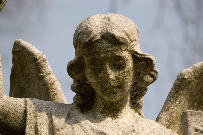 The worn face of an angel statue, with a sad expression.