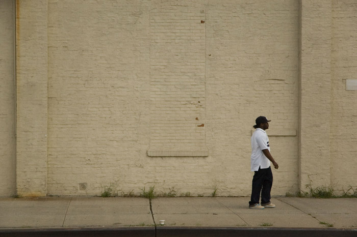 A solitary pedestrian, dwarfed by a monolithic brick wall.