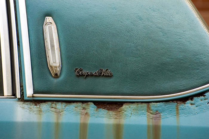 The body of a blue Coupe de Ville is streaked with rust.
