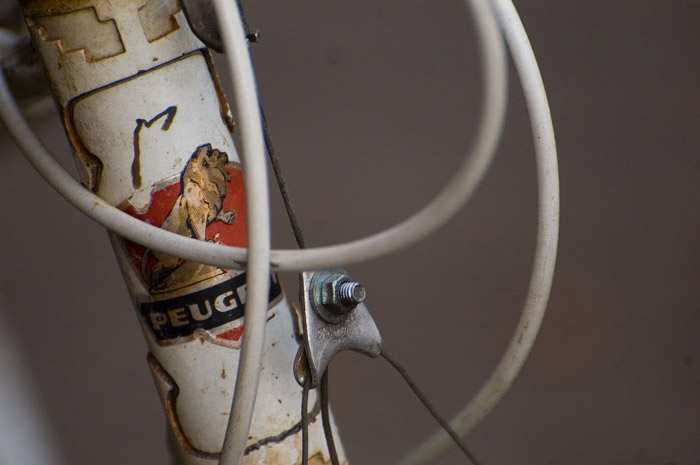 An old white bike, its brake cables obscuring the Peugeot logo.