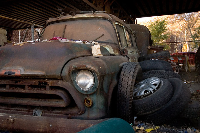 An old Chevy shows years of neglect, surrounded by trash.