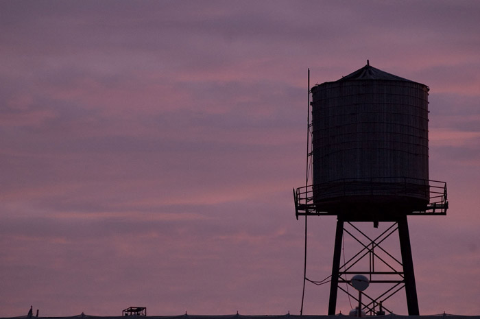 A water tank and its supporting structure in silhouette against a purple sky.
