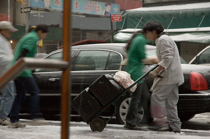 A worker pushes a cart on a slush-filled sidewalk while others duck from the snow and rain.