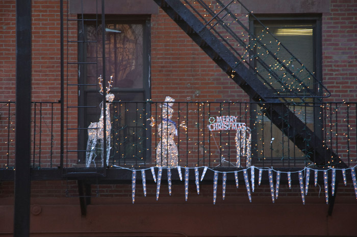 A fire escape is festooned with Christmas decorations: lit icicles, a reindeer, a snowman, and 'Merry Christmas.'