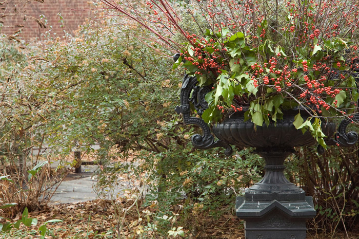A large pot, on a pedestal, has am arrangement featuring red berries.