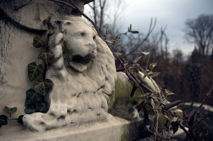 A worn statue of a lion, with surrounding vines, and a dark sky in the background.