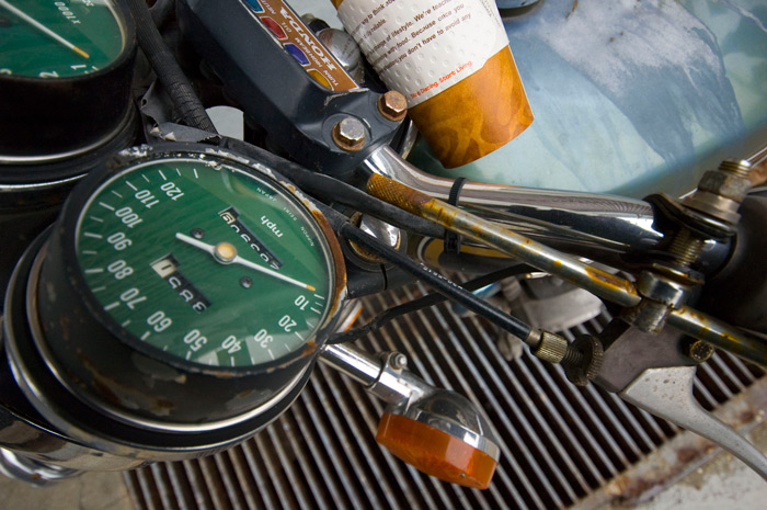 A Honda motorcycle's handlebars are surrounded by gauges and an empty coffee cup.