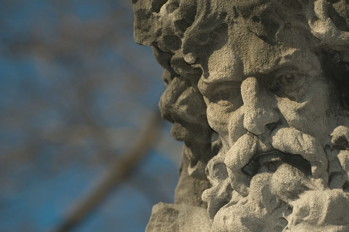 A statue's face, with heavy beard and mustache, has a somber expression.
