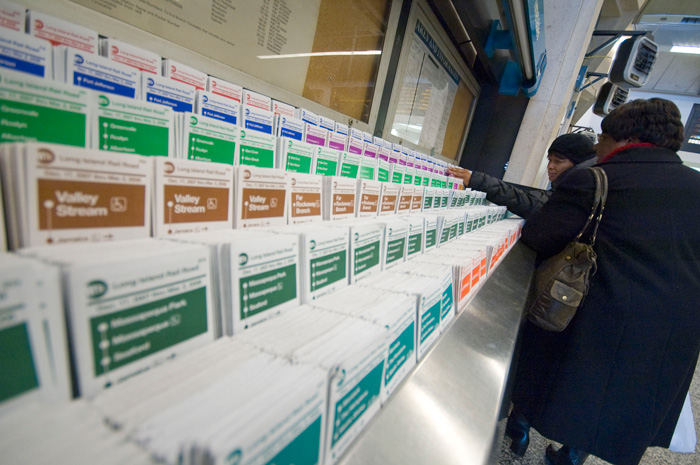 Two people look over a rack filled with Long Island Rail Road time tables.
