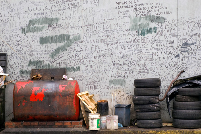 A grey wall has spare tires at its base, but the wall has been scrawled with hundreds of names of policians and celebrities.