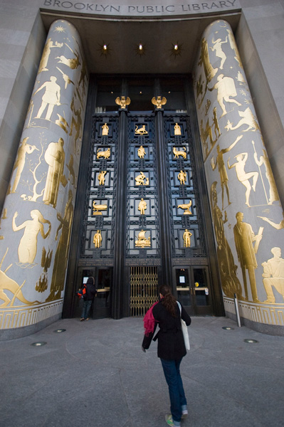 A woman approaches a gilded library entrance, with pillars and doors decorated with symbols of the humanities.