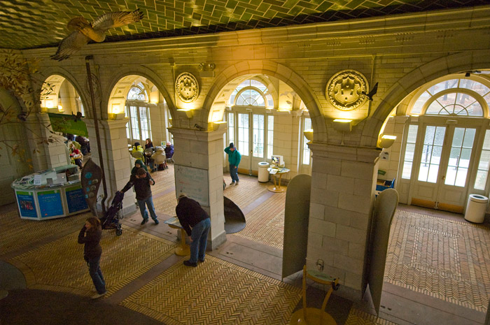 People congregate in two rooms with elaborately tiled floors and ceilings, separated by arched walkways.