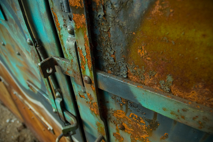 An old fire door was painted in psychedelic colors, but the paint is peeling and rust is showing through.