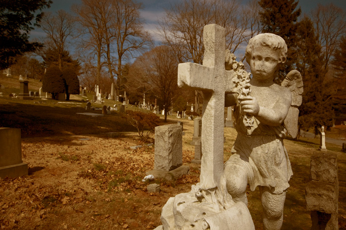 A sculpture shows a young angel placing a wreath on a cross over a grave.