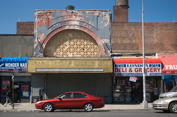 A red car sits in front of an old, dilapidated theater.