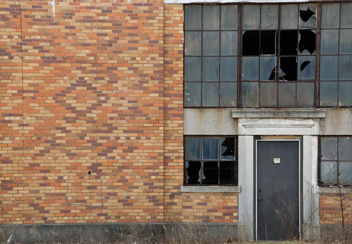 A black door leads into an old airplane hangar, many of whose window panes are broken or missing.
