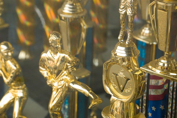 A store window has a trophies for karate, basketball, and baseball.