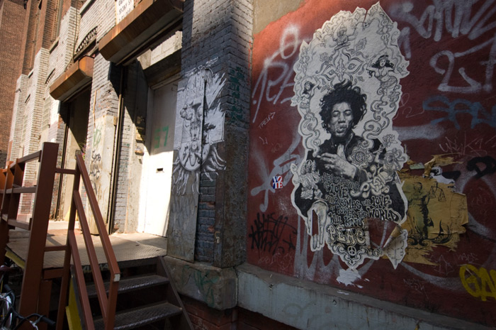 A black and white, psychedelic paste-up poster of Jimi Hendrix is on a wall next to an industrial doorway.
