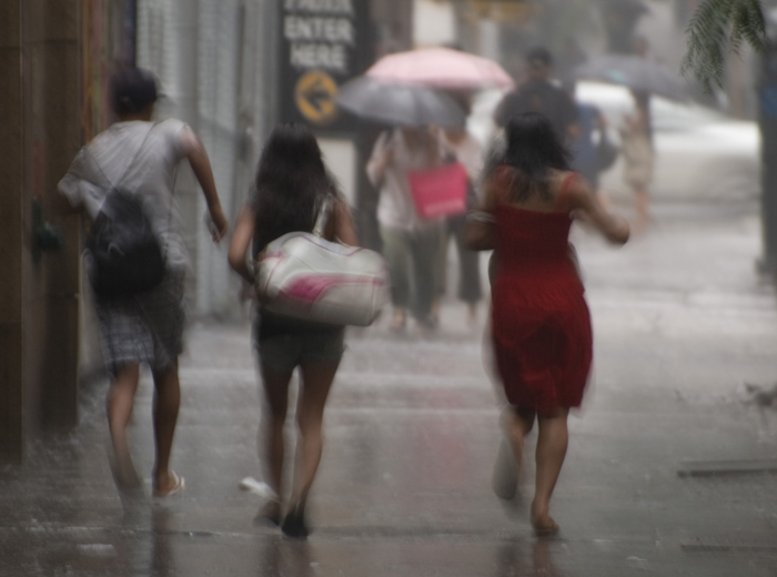 Three people run through the street, in a blur, trying to escape heavy rain.