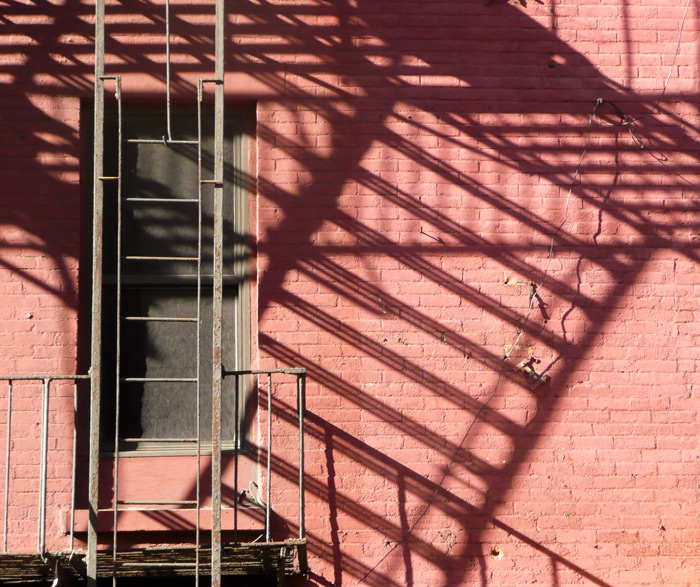 A fire escape's landings cast diagonal shadows on a red brick building.