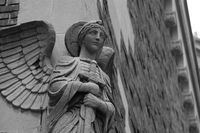 A statue of a guardian angel, with wings spread and clutching an unraised sword, adorns the corner of a church.