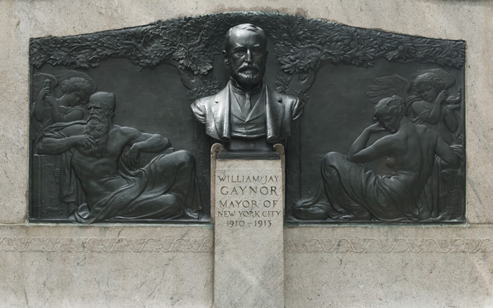 A bust of a former mayor of New York City is in front of a bas relief, with figures of 'Strength,' 'Knowledge,' and 'Ease.'