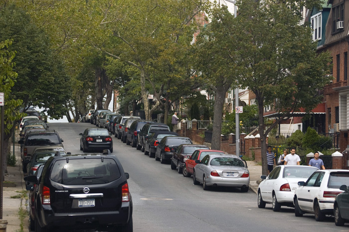 A tree-lined street on a residential block has a gentle rolling hill.