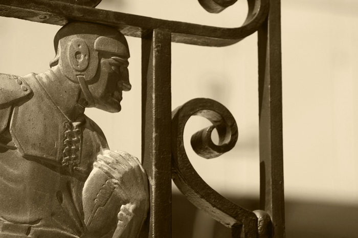 An iron gate is decorated with the figure of an early era football player, clutching a football.
