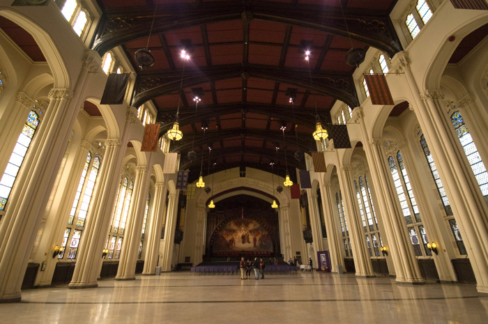 The picture shows a large hall, at least two stories tall, with stained glass windows and pillars on each side.