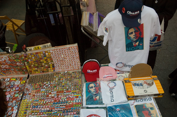 A table in a market has t-shirts and baseball caps decorated with Barack Obama designs.