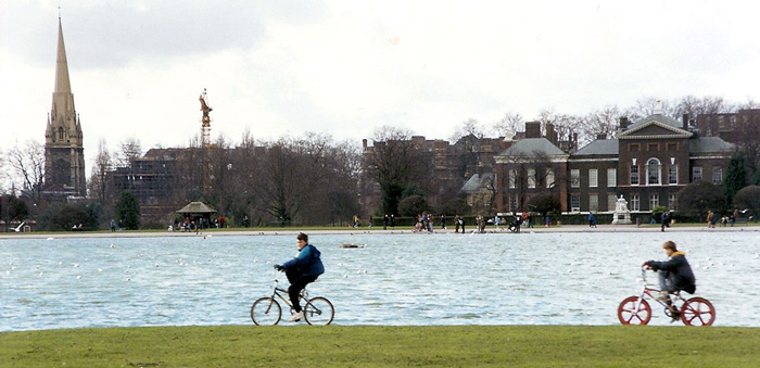 Two teenagers ride their bikes by a lake in London's Hyde Park.