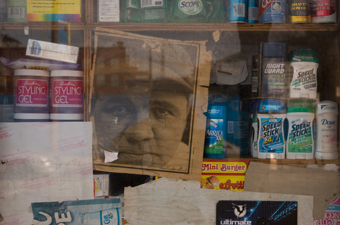 A faded newspaper page of Babe Ruth's face stares out amidst deodorants and other health and beauty aids in the window of a small bodega.