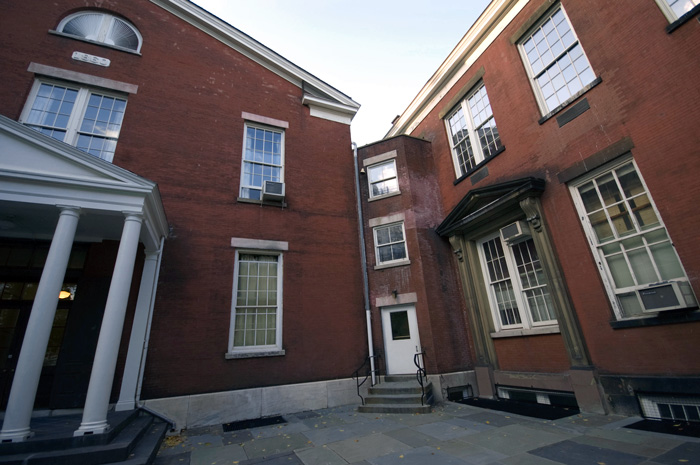 Two old brick buildings converge at a right angle to a door in a joining section.