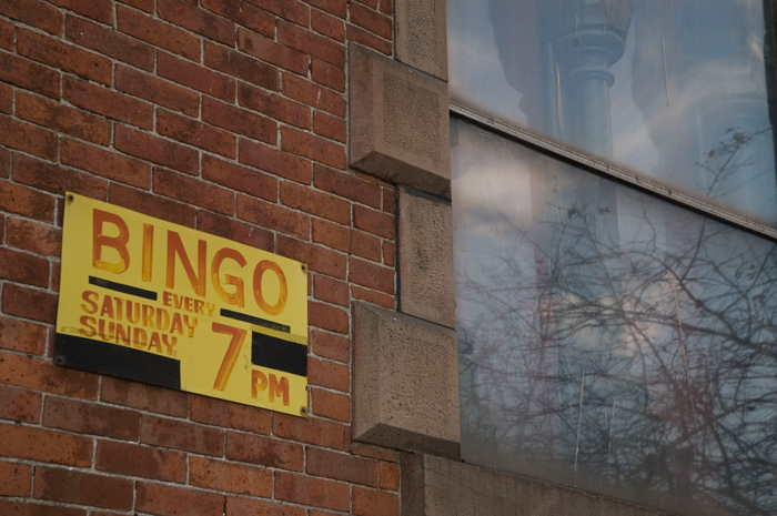 A yellow sign on a brick wall reads out the hours for the church Bingo.