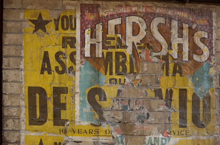 The picture shows layered old signs for food and an assembly man.