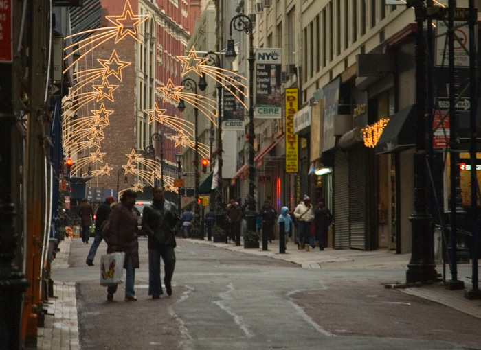As dusk falls on a pedestrian street, holiday lights create a canopy overhead.