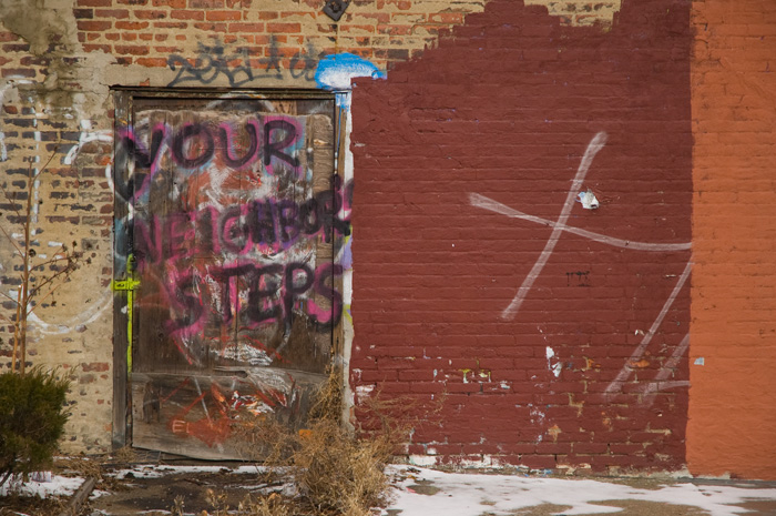 A wall and door have been repainted several times to ward off graffiti, with a reminder that people live here.