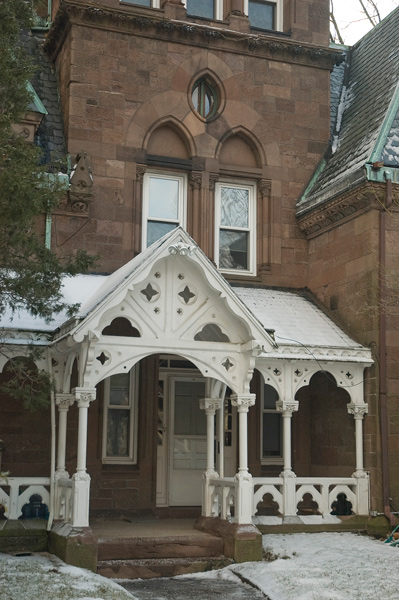 A white wooden porch leads to a stately building made out of brownstone.